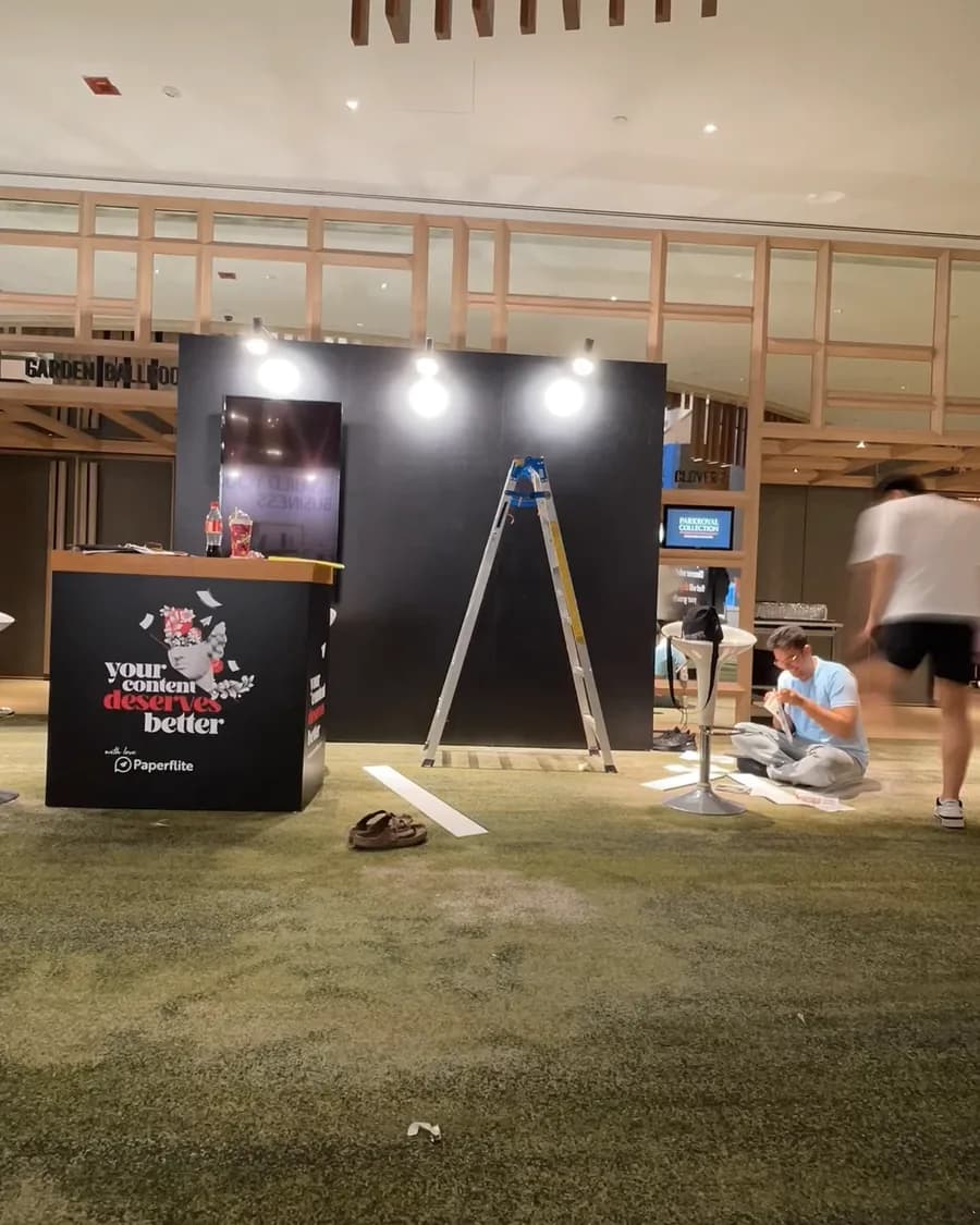 The booth at an event: a black stall and a ladder under the hall's timber ceiling, still being set
