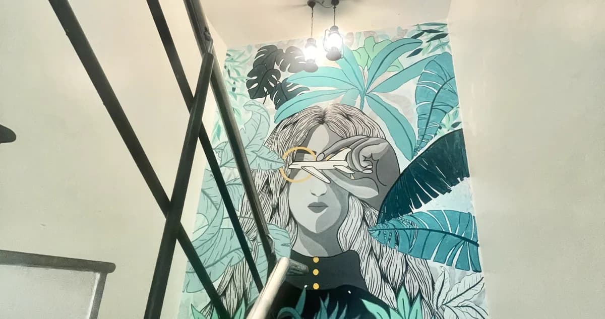 The mural on the office stairwell: a woman's face among palm leaves, in teal and white