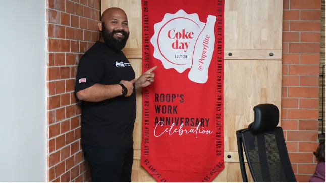 Roop beside a red banner for Coke day, his work anniversary
