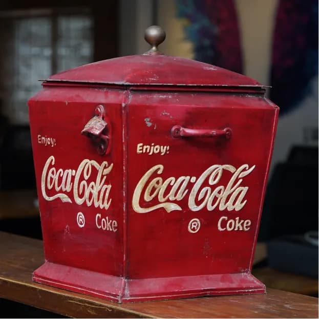 A worn red Coca-Cola cooler on a wooden counter